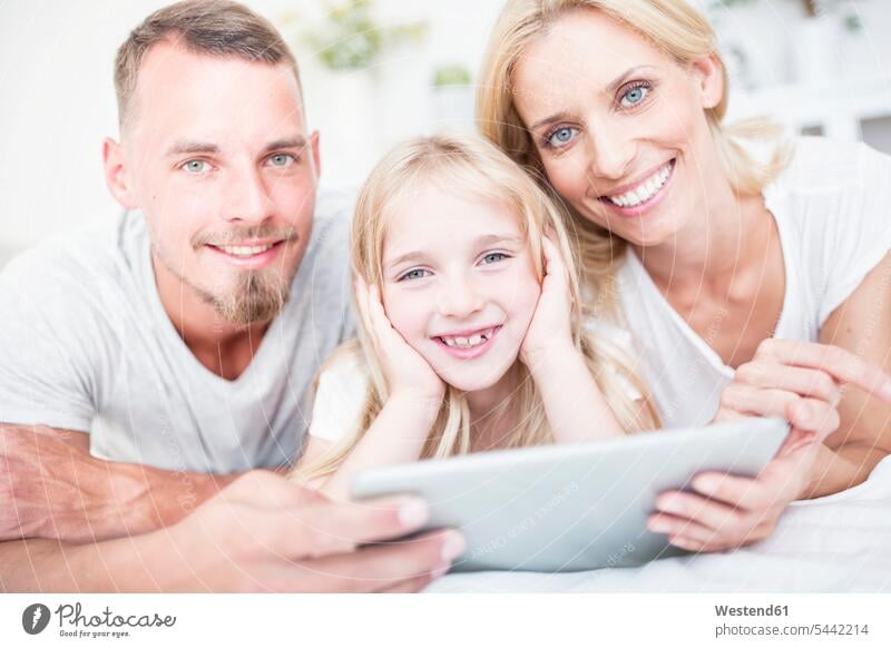 Portait of smiling girl with parents lying in bed with tablet daughter daughters smile beds family families digitizer Tablet Computer Tablet PC Tablet Computers