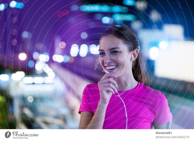 Smiling young woman in pink sportshirt listening to music in city at night young women on the phone call telephoning On The Telephone calling talking speaking