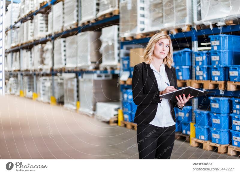 Blond businesswoman standing in storehouse, writing in notebook storage warehouse manager female managers notebooks write inventory stocktaking stock control