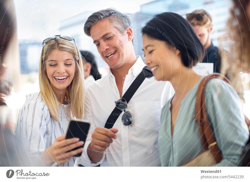Group of casual businesspeople sharing cell phone on urban square mobile phone mobiles mobile phones Cellphone cell phones colleagues smiling smile telephones