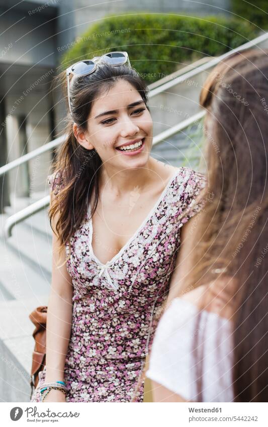 Two smiling young women talking in the city female friends speaking smile mate friendship woman females Adults grown-ups grownups adult people persons