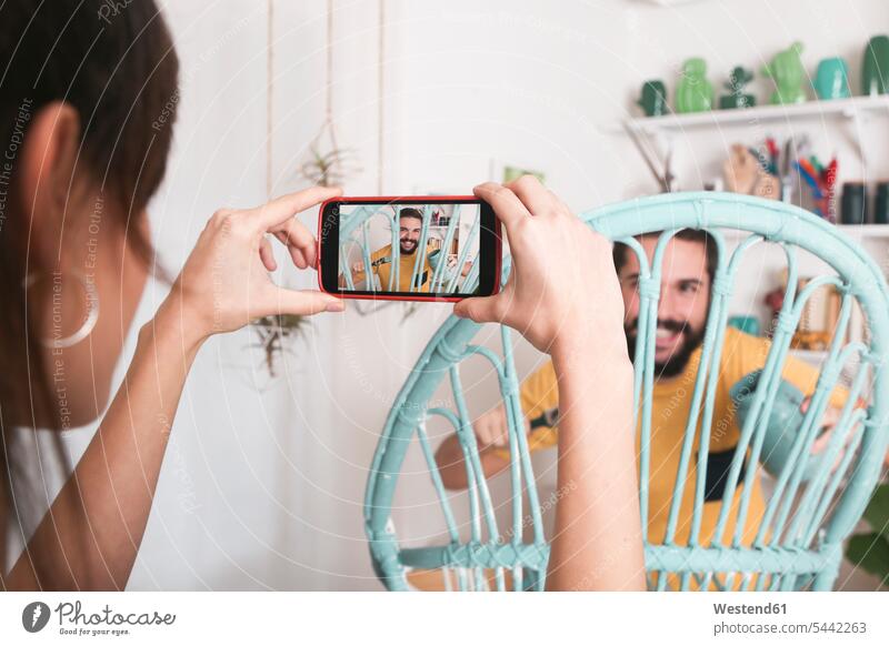 Young woman taking photo of bearded man painting wicker armchair at home mobile phone mobiles mobile phones Cellphone cell phone cell phones photographing