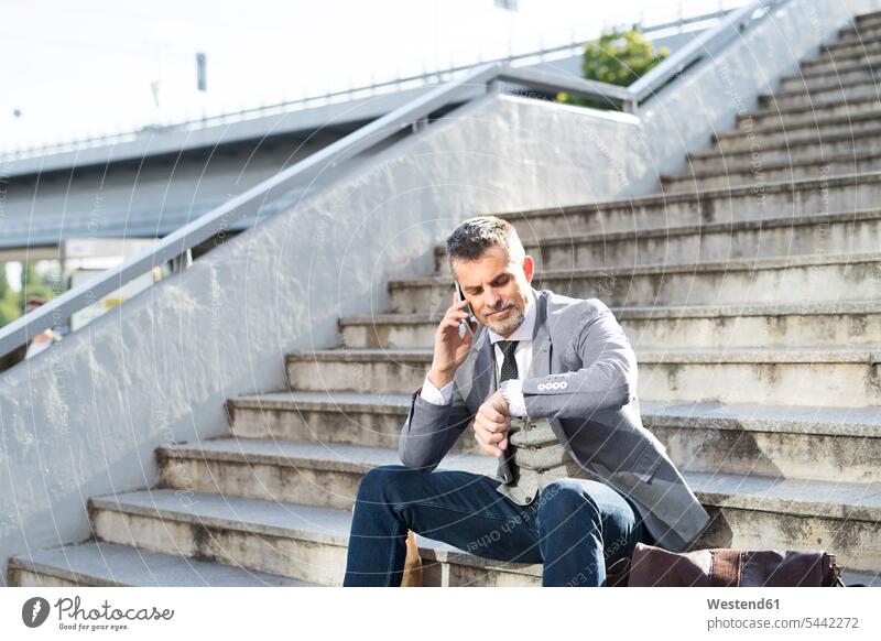 Businessman in the city sitting on cell phone checking the time Business man Businessmen Business men break stairs stairway business people businesspeople