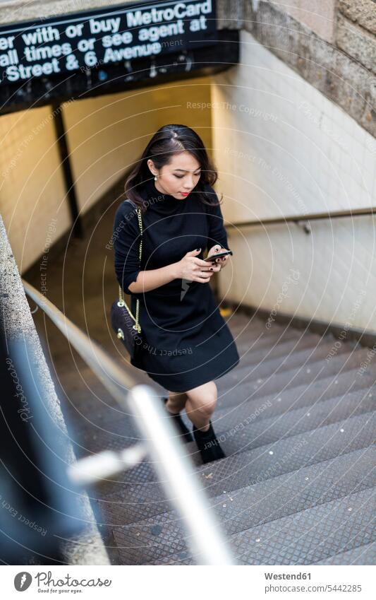 USA, New York City, Manhattan, young woman dressed in black walking upstairs looking at cell phone females women Smartphone iPhone Smartphones Adults grown-ups