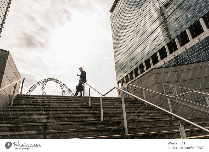 Businessman leaning on railing on top of stairs reading messages text messaging SMS Text Message career Success successful Smartphone iPhone Smartphones urban