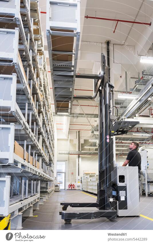 Worker operating forklift in factory warehouse man men males forklifts forklift truck forklift trucks storehouse storage working At Work worker