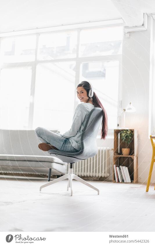 Young woman making a video call from her mobile phone, wearing headphones music loft lofts chair chairs mobiles mobile phones Cellphone cell phone cell phones