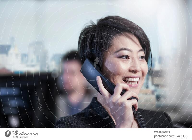 Smiling woman in office talking on phone smiling smile females women on the phone call telephoning On The Telephone calling businesswoman businesswomen