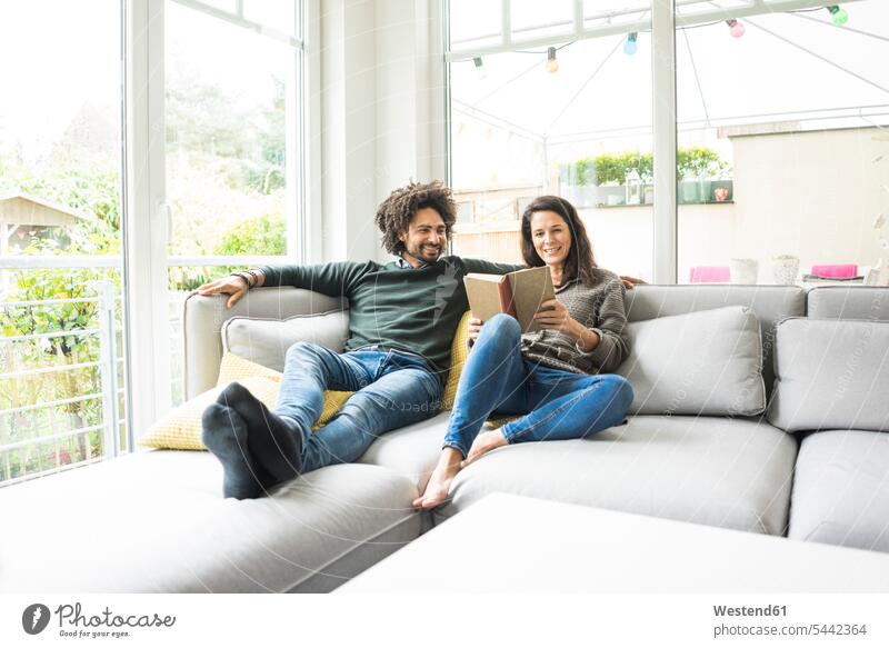 Couple sitting on couch reading book couple twosomes partnership couples settee sofa sofas couches settees Seated people persons human being humans human beings
