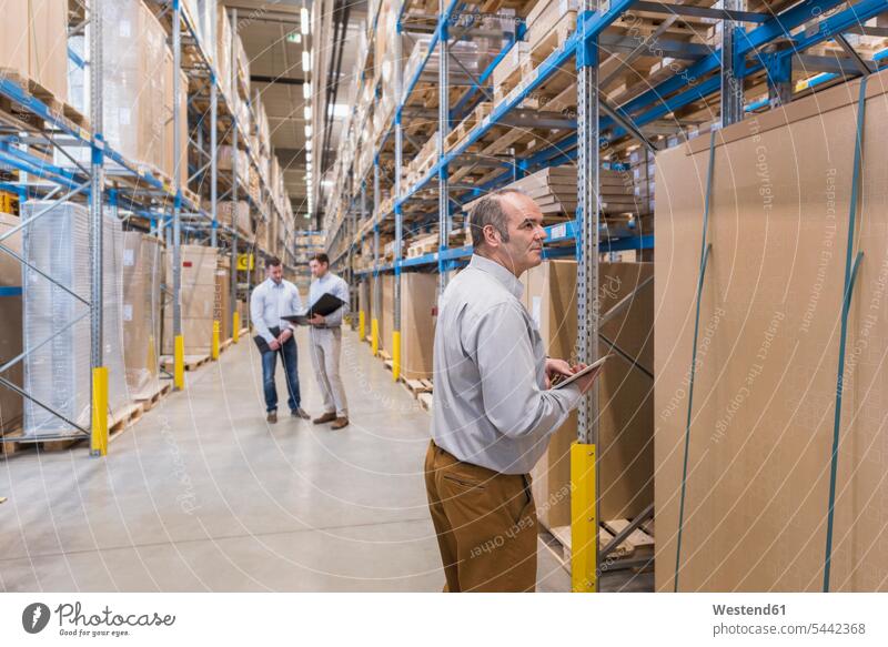 Man with tablet and two men with folder in factory warehouse man males storehouse storage working At Work colleagues talking speaking Adults grown-ups grownups
