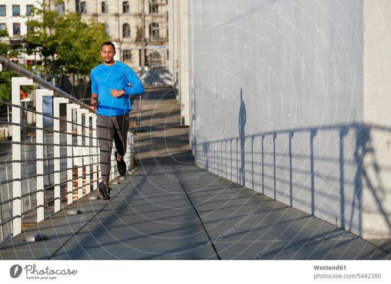 Young man running on footbridge in the city men males Jogging exercising exercise training practising Adults grown-ups grownups adult people persons human being