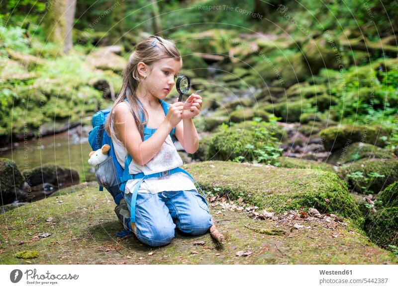 Little girl with magnifier crouching on rock in the woods watching a feather looking looking at females girls magnifiers magnifying glasses view seeing viewing