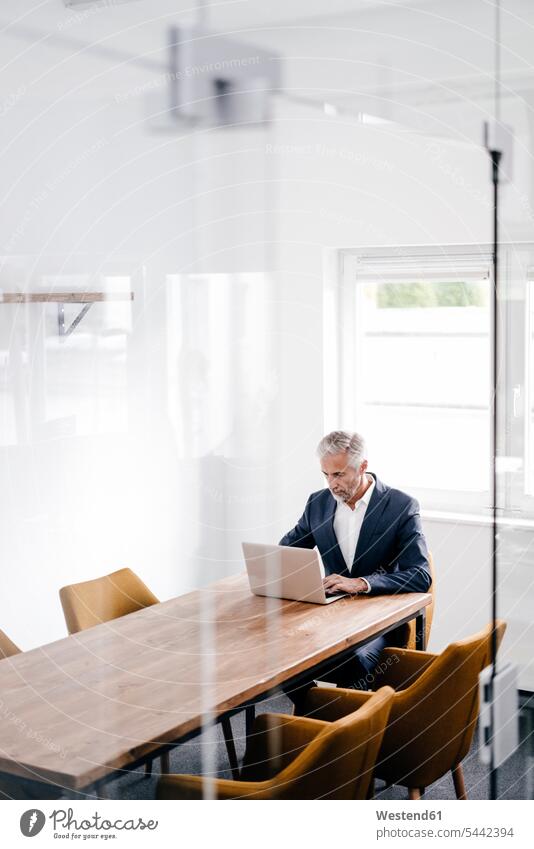 Mature businessman using laptop on conference table in office Businessman Business man Businessmen Business men offices office room office rooms sitting Seated