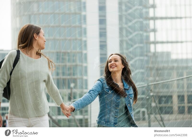 Two girlfriends walking in the city, holding hands female friends going laughing Laughter cheerful gaiety Joyous glad Cheerfulness exhilaration merry gay