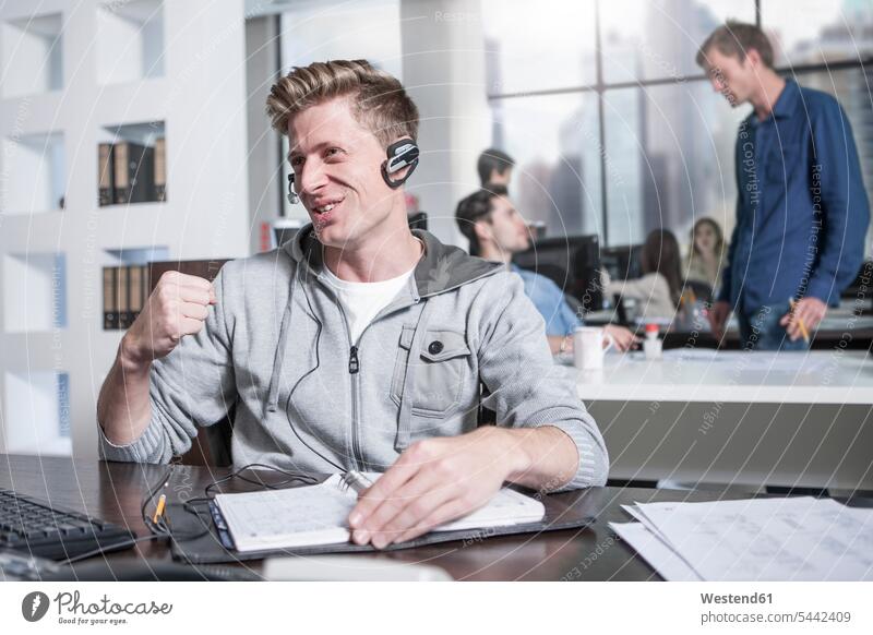 Young man at desk in office wearing a headset headsets offices office room office rooms men males on the phone call telephoning On The Telephone calling