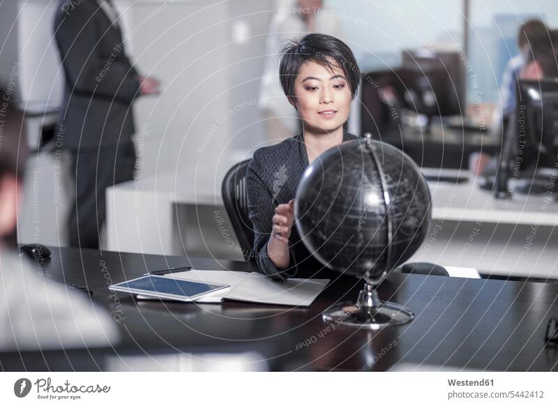 Woman looking at globe sitting at desk in city office offices office room office rooms globes workplace work place place of work business business world