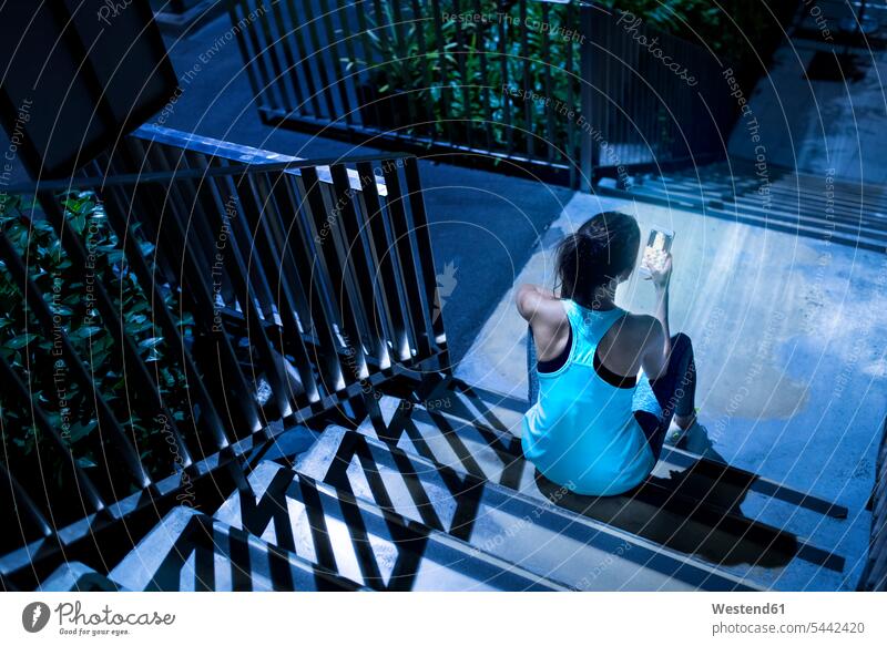 Young woman sitting on stairs and checking her smartphone in modern urban setting at night Smartphone iPhone Smartphones exercising exercise training practising