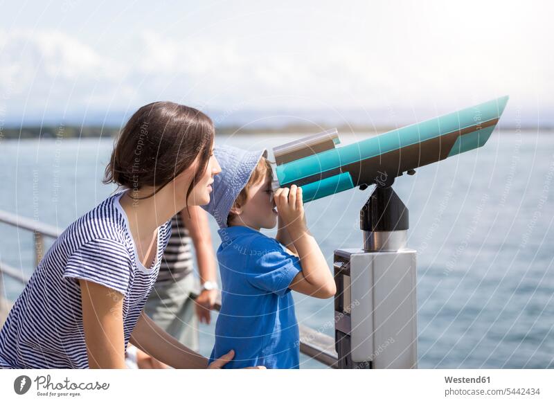Germany, Friedrichshafen, Lake Constance, mother with son looking through telescope at lakeshore sons manchild manchildren mommy mothers mummy mama water waters