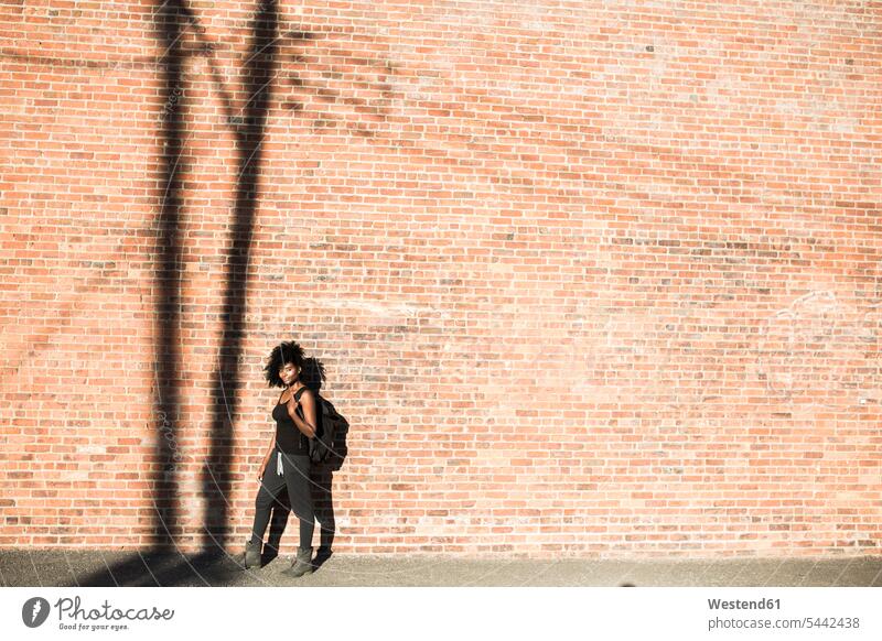 Woman with backpack in front of brick wall with shadow of a power pole standing woman females women brick walls Adults grown-ups grownups adult people persons