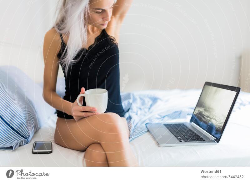 Young woman in bed with cup of coffee and laptop Coffee Laptop Computers laptops notebook Coffee Cup Coffee Cups beds females women Drink beverages Drinks