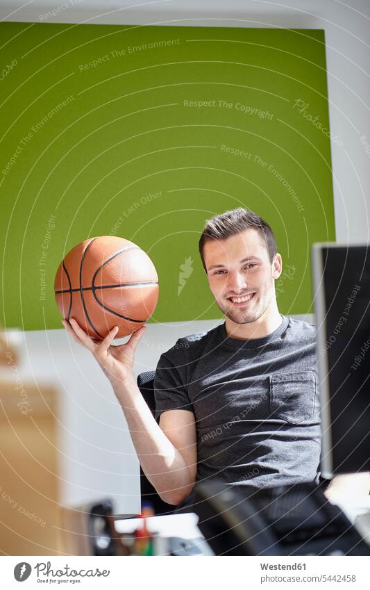 Young man working in office, balancing a basketball At Work portrait portraits balls balance offices office room office rooms smiling smile sitting Seated