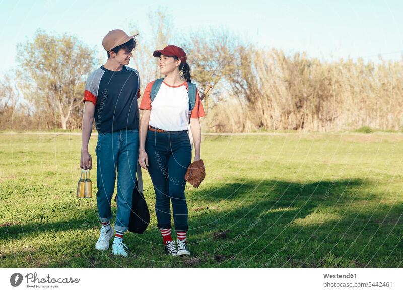 Smiling young couple with baseball equipment walking in park smiling smile twosomes partnership couples baseball player baseball players sport sports people