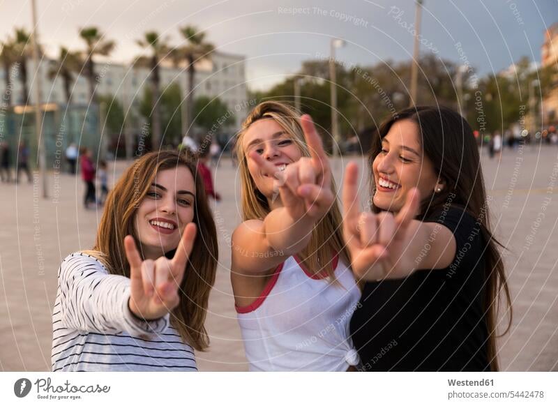 Spain, Barcelona, three happy young women showing Rock And Roll Sign female friends mate friendship Sign of the Horns Horn Signs woman females portrait