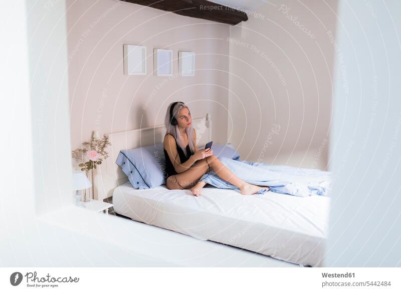 Young woman in bed with cell phone and headphones beds mobile phone mobiles mobile phones Cellphone cell phones females women headset telephones communication