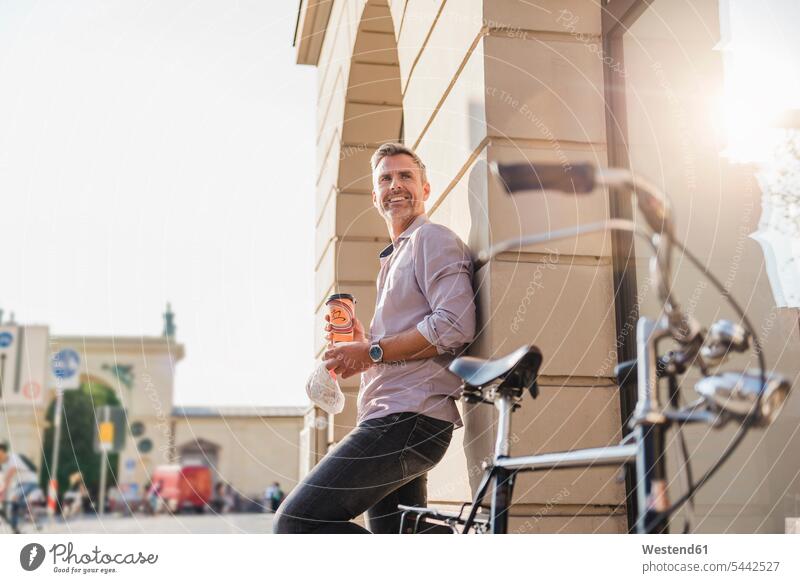 Smiling man with bicycle and takeaway coffee in the city town cities towns smiling smile bikes bicycles men males Coffee outdoors outdoor shots location shot