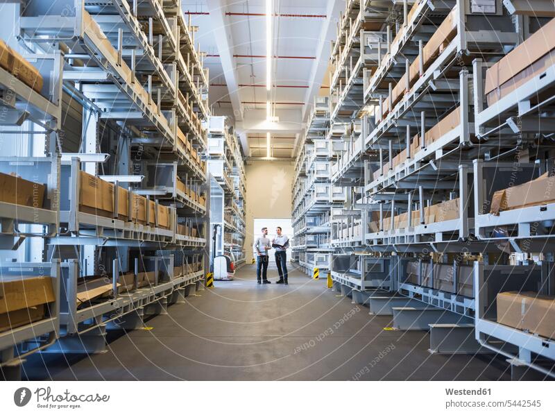 Two men standing in factory warehouse man males colleagues storehouse storage working At Work Adults grown-ups grownups adult people persons human being humans