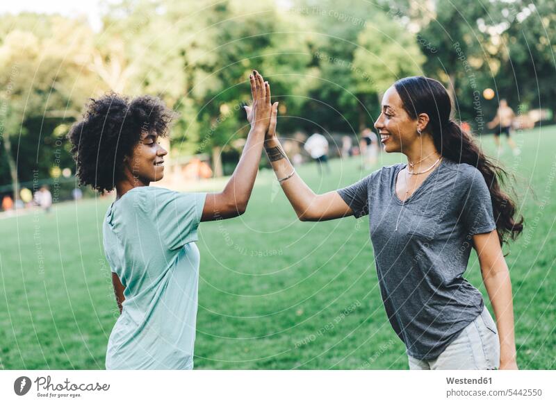 Two young woman high fiving in a park High Five Hi-Five high-fiving High-Five parks female friends mate friendship best friend bff best friends standing females