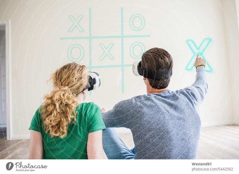 Young couple wearing VR glasses playing virtual tic tac toe twosomes partnership couples flat flats apartment apartments people persons human being humans