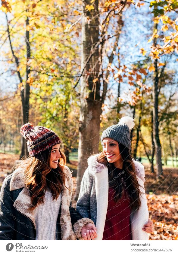 Two pretty women smiling at each other in an autumnal forest female friends woman females smile beautiful fall woods forests mate friendship Adults grown-ups