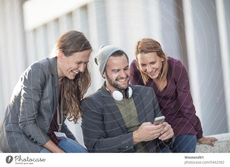 Three happy young people looking at cell phone together colleagues mobile phone mobiles mobile phones Cellphone cell phones laughing Laughter telephones