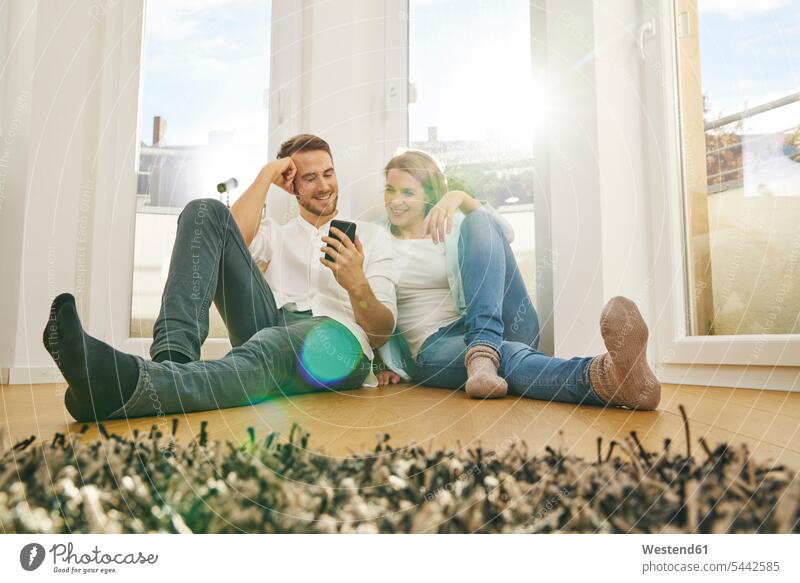Smiling couple sitting on floor looking at cell phone smiling smile mobile phone mobiles mobile phones Cellphone cell phones twosomes partnership couples