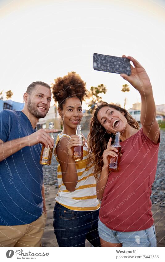Three friends with beer bottles taking selfie on the beach beaches Selfie Selfies friendship photographing Smartphone iPhone Smartphones Beer Bottle