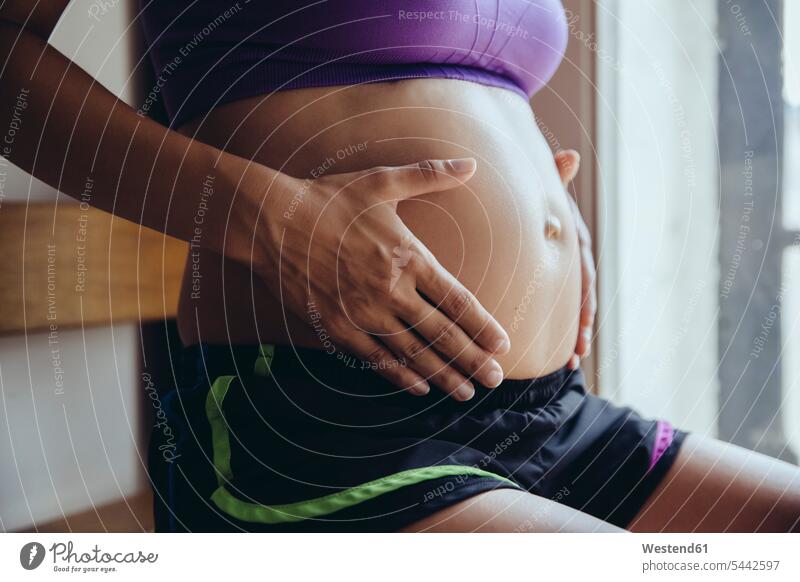 Sporty pregnant woman holding her belly sitting Seated bellies abdomen human abdomen females women Pregnant Woman people persons human being humans human beings