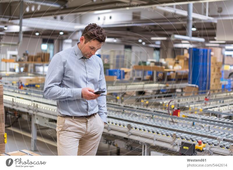 Man at conveyor belt in factory looking at cell phone mobile phone mobiles mobile phones Cellphone cell phones storehouse storage warehouse Businessman