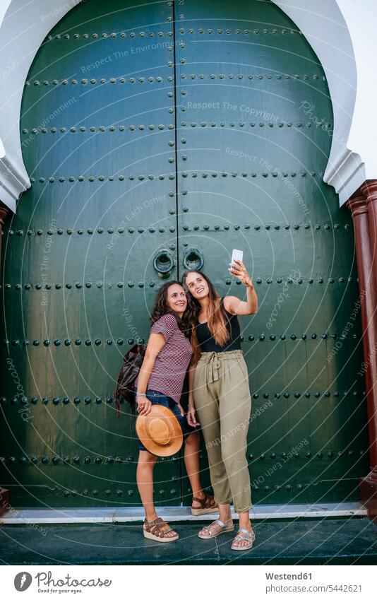 Morocco, Chefchaouen, two women taking selfie with smartphone in front of green portal Selfie Selfies portals woman females Smartphone iPhone Smartphones colour