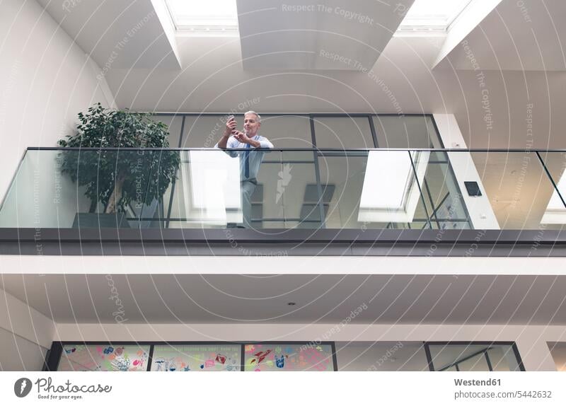 Successful businessman standing at railing in his office, using smartphone text messaging SMS Text Message Businessman Business man Businessmen Business men