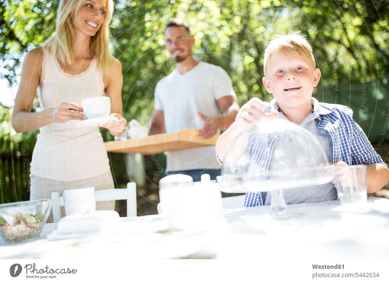 Smiling boy with his parents laying garden table boys males family families son sons manchild manchildren smiling smile Table Tables kid kids people persons