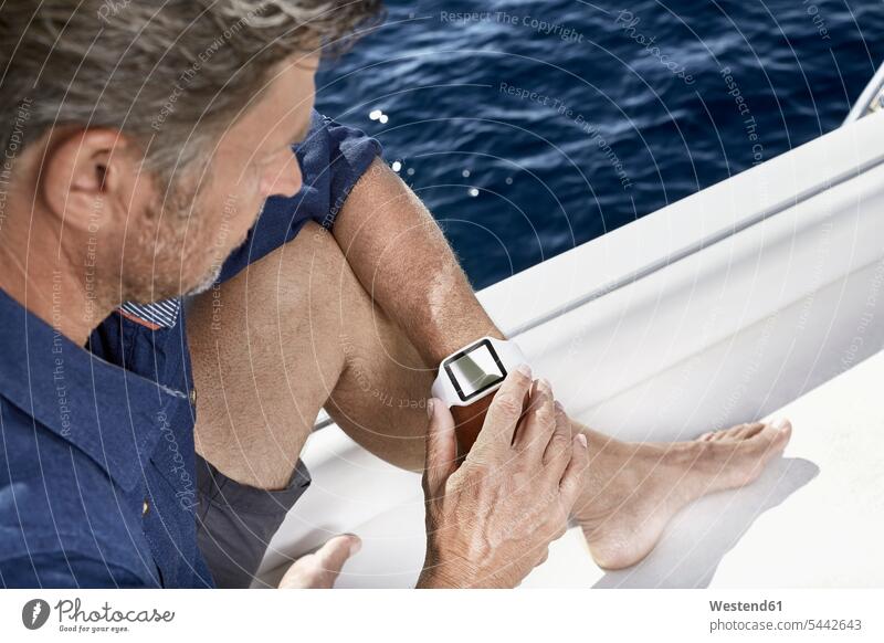 Man sitting on motor yacht looking at his smartwatch man men males motor yachts smart watch Adults grown-ups grownups adult people persons human being humans