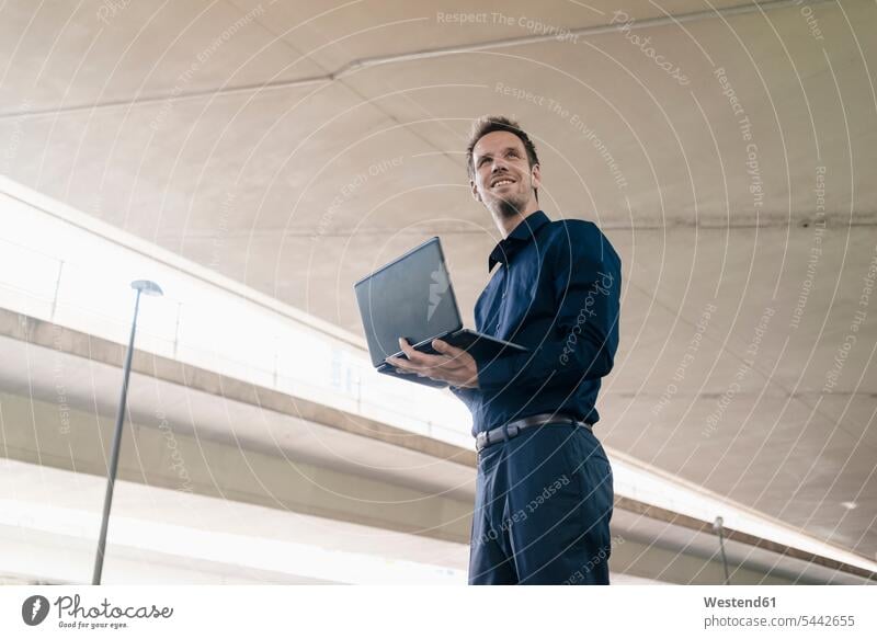 Confident businessman standing at underpass using laptop Laptop Computers laptops notebook smiling smile Businessman Business man Businessmen Business men