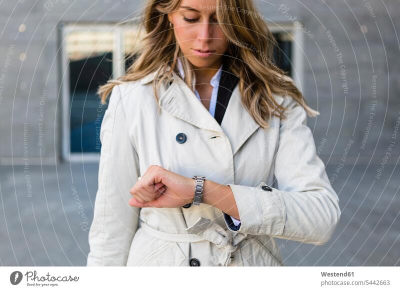 Businesswoman checking the time businesswoman businesswomen business woman business women trenchcoat trench coat business people businesspeople business world