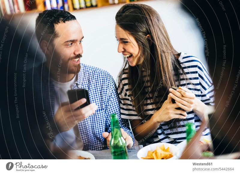 Happy couple sharing cell phone at dining table mobile phone mobiles mobile phones Cellphone cell phones Table Tables twosomes partnership couples eating