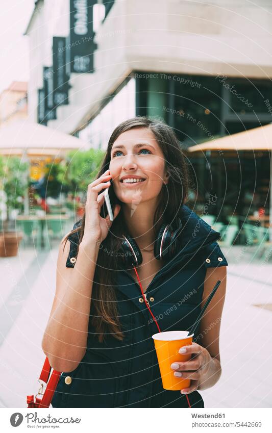 Portrait of smiling young woman on cell phone with takeaway drink in the city females women mobile phone mobiles mobile phones Cellphone cell phones smile