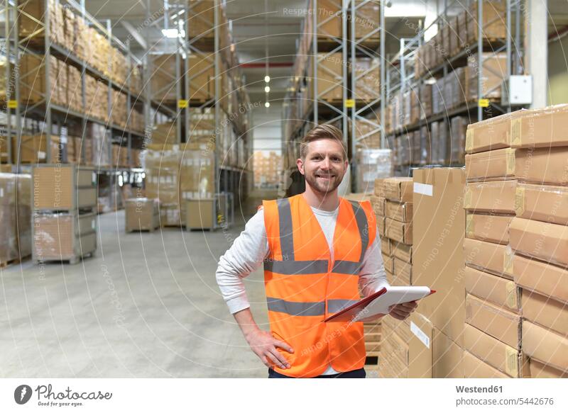 Portrait of smiling man in factory hall wearing safety vest holding clipboard smile men males working At Work storehouse storage warehouse Adults grown-ups