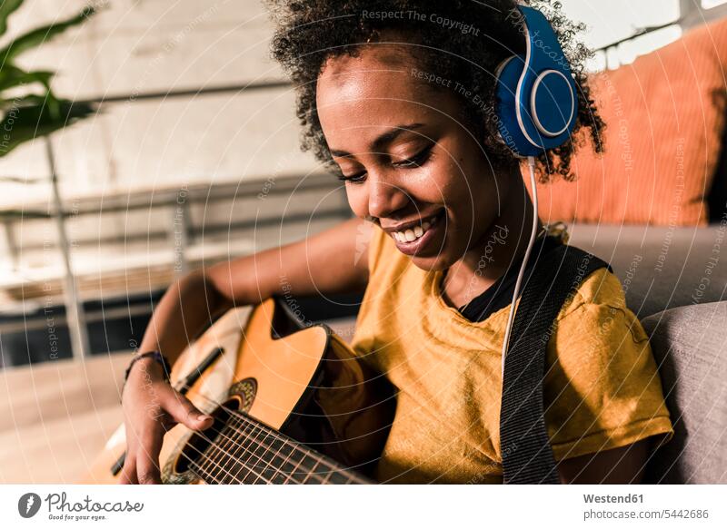 Smiling young woman at home with headphones playing guitar smiling smile females women guitars headset Adults grown-ups grownups adult people persons
