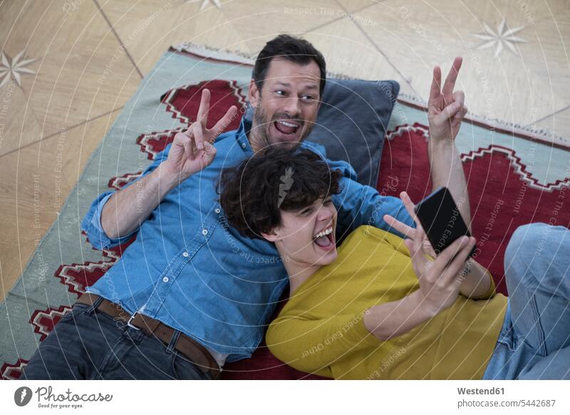 Couple lying together on the carpet taking selfie with smartphone Selfie Selfies couple twosomes partnership couples people persons human being humans