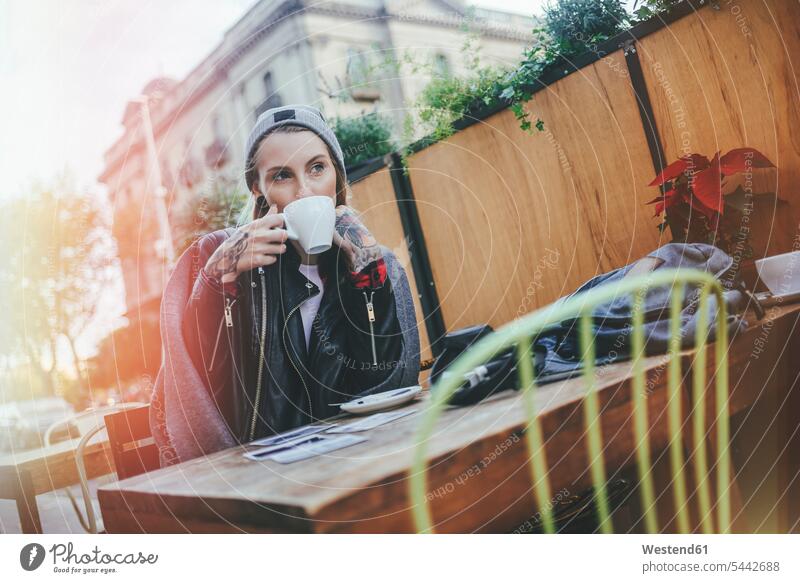 Young tattooed woman sitting in pavement cafe drinking coffee outdoor cafes females women Adults grown-ups grownups adult people persons human being humans